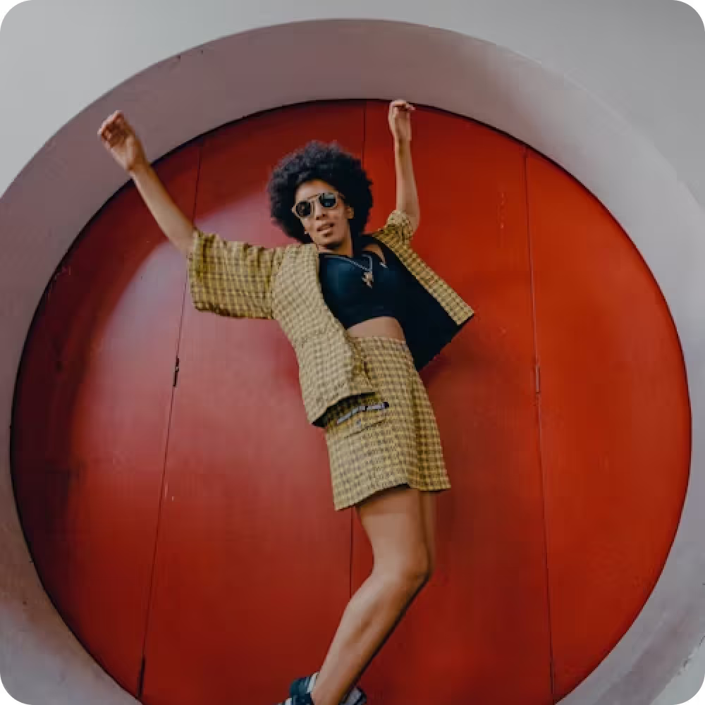 Image of a woman wearing a yellow skirt and jacket stands confidently in front of a circular door, showcasing her vibrant style.